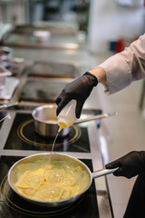 Chef of the restaurant add an olive oil on frying pan with raviolli pasta in curry sauce. Smooth image with shallow depth of field.