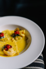 Plate of raviolli pasta with shrimps, salmon and curry sauce. Dark background. Smooth image with shallow depth of field.