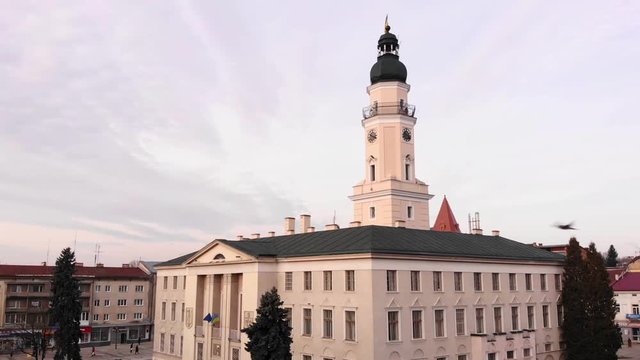City Hall of Drohobych city on the central square, doves flying around.  Blue and yellow the flag of Ukraine on the spire. Ancient European city of Drohobych. Interesting places in Ukraine