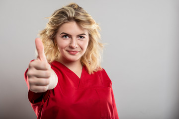 Portrait of female nurse wearing red scrub showing thumb up