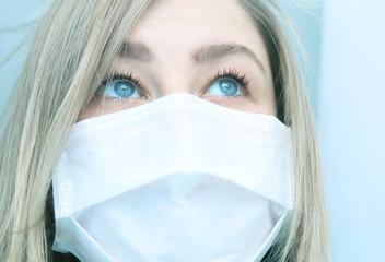 Young woman with light hair and blue eyes is covered with a medical protective mask. Selective focus. The epidemic of coronavirus. Covid19 prevention