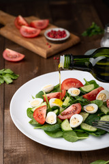 Salad with spinach, cucumber, tomato and quail egg on a white plate on a wooden background, pours Olive Oil