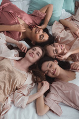 Top view of multiethnic women smiling and resting on bed at bachelorette party