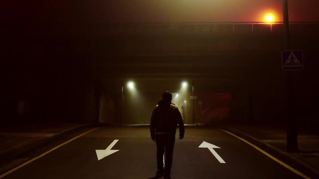 unrecognizable adult man walks alone on a foggy road at night.