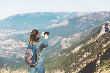 Tourist girl making a photo shoot of mountain. Young beautiful girl travels alone in the mountains in spring or autumn, looks into the distance and enjoys nature, rocks and green forests, view of the