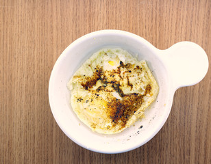 Two eggs cooked in a microwave, well done, in a small white dish, on a light wooden background.