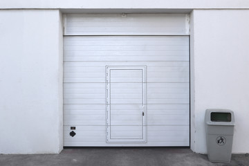closed white garage or warehouse front with door entrance and a bin for recycling