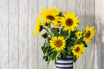 A bunch of sunflowers in a black vase on a rustic white wooden table