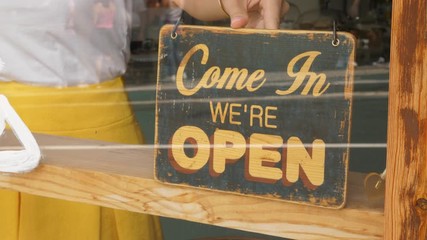 Woman turn 'open' sign in the window of small cafe, closeup shot. End of break or start of workday at small store or tea house at European town