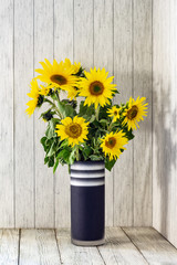 Fototapeta premium A bunch of sunflowers in a black vase on a rustic white wooden table