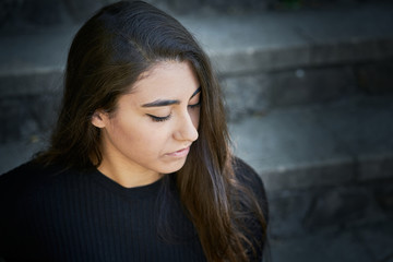 Portrait of a young woman dressed in a sweater and black trousers and in the background you can see the handrail of some stairs.