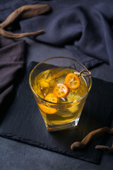 Glass of strong alcohol, whiskey, ice, kumquat on a table
