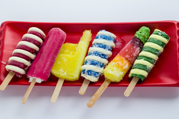 Colorful stick ice creams on the red long plate on white.