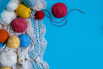 Scattered colored balls of thread and a knitted tablecloth on a blue background. Flat layout with...