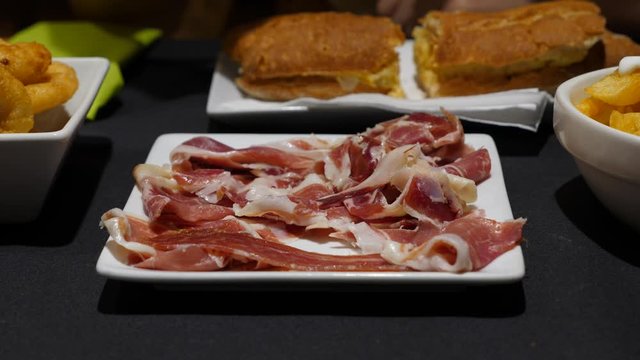 Pick up thin jamon from plate, typical tapa at Spanish restaurant, closeup shot. Tasty dry-cured ham thin slices