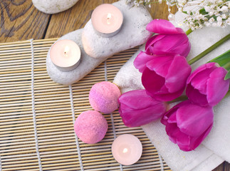 Fototapeta na wymiar Romantic spa flatlay with bath bomb, tulips, candles and pebbles on bamboo mat. Resort concept for Valentines day, Mothers day or wedding greeting card.