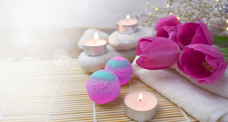 Romantic spa with bath bomb, tulips, candles and pebbles on wooden background.  Resort concept for Valentines day, Mothers day or wedding greeting card. Copyspace