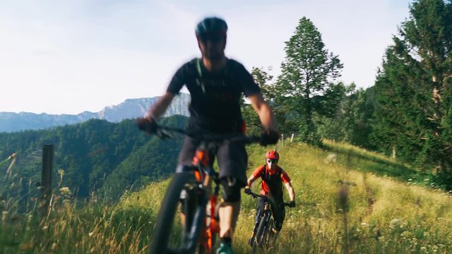 Two men biking riding downhill on a mountain bike trough the forest trails slow motion