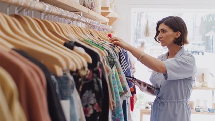 Female owner of fashion store using digital tablet to check stock on rails in clothing store - shot in slow motion - Powered by Adobe