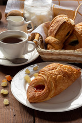 A variety of puff pastry buns with cherries, kiwi, apricot. Rolls, croissants with various fillings. A Cup of coffee with milk, Breakfast. Still-life.