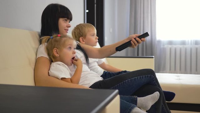 Happy family mom and two children are sitting on the couch in front of the TV. Smart TV switching remote control in the hands of a girl. Family watching television. Modern technology concept