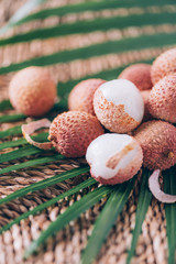 Lychee fruits with palm leaves on rattan background. Copy space. Exotic litchi, lichee fruits. Tropical food concept.