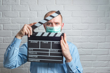 Man in blue shirt in virus mask on white with clapperboard