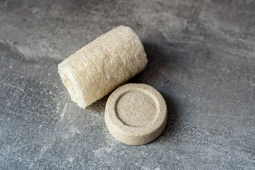 Beige solid soap bars or shampoo and loofah on grey background. Eco bathroom accessories, zero waste cosmetics products, plastic free lifestyle concept