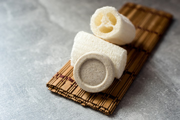 Beige solid soap bars or shampoo and loofah on wooden stand grey background. Eco bathroom accessories, zero waste cosmetics products, plastic free lifestyle concept