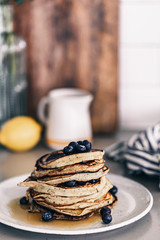 Lemon poppy seed pancakes on grey plate. Fresh blueberries on top. Maple syrup drizzle. Stack of warm pancakes. Breakfast brunch time. Kitchen countertop. Lifestyle food photography. Fluffy pancakes.