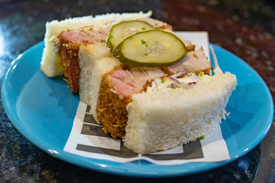 P&atilde;o recheado com barriga de porco e salada de repolho com picles dentro de um prato azul em fundo escuro de marmore  Katsu Sando de Barriga Suina  Salada Coleslaw  molho chuno 