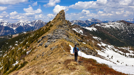 Fototapeta na wymiar A man with big hiking backpack hiking to Himmeleck peak, Austria. There is a massive mountain range in the back, partially covered with snow. Early spring vibes. Freedom and adventure.