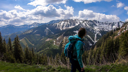 Obraz premium A woman with big hiking backpack hiking to Himmeleck peak, Austria. There is a massive mountain range in the back, partially covered with snow. Early spring vibes. Freedom and adventure.