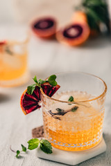 Summer cocktail in rock glass. Whiskey glass. Citrus fancy cocktail with ice. Blood orange decoration with fresh mint. Refreshing summer cocktail on white table. Cocktail silver shaker. Yellow color.