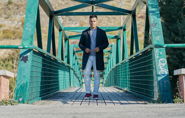 portrait of a handsome Hispanic boy walking on a metal pedestrian bridge with good pants and urban clothing: jeans, blue shirt and dark jacket and sunglasses on the face