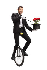 Smiling magician iding a unicycle and holding wand and hat with flowers © Ljupco Smokovski