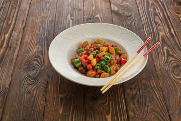 Chinese food, kung pao chicken in white plate with chopsticks on wooden table