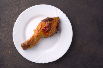 Roasted chicken leg on a white plate. View from above.