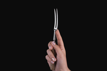 Female hand holds a fork for meat on a black background.