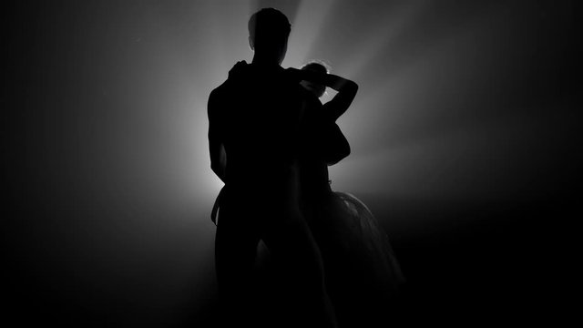 Romantic professional ballet pair practicing moves on dark stage. Young couple dancing in classic dress, spinning around and smiling. Gracefulness and tenderness in every movement.