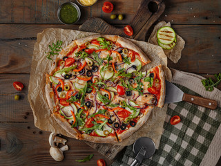 tasty pizza for vegetarians on a rustic wooden table with vegetables baked with zucchini, black olives, green olives, peppers and tomatoes, top view