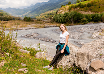 Naklejka na ściany i meble Mountain river landscape. Ecotourism, travel concept and discovery of beautiful places. Attractive young woman sitting by a mountain stream