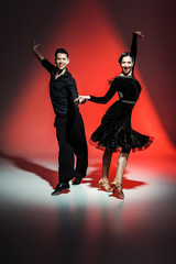 elegant young couple of ballroom dancers in black outfits dancing in red light