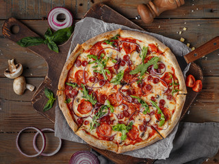 pizza on a wooden table with parmesan and arugula, sausages and champignons, top view