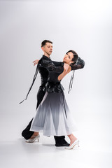 Fototapeta premium elegant young couple of ballroom dancers in black outfit dancing on white