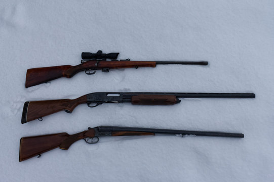 top view of rifle, double barrel shotgun and pump action shotgun in the snow