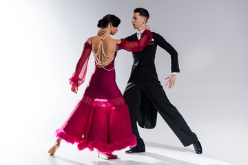 elegant young couple of ballroom dancers in red dress in suit dancing on white
