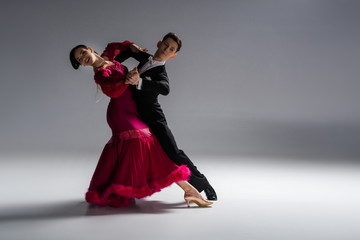 elegant young couple of ballroom dancers in red dress in suit dancing on grey - obrazy, fototapety, plakaty