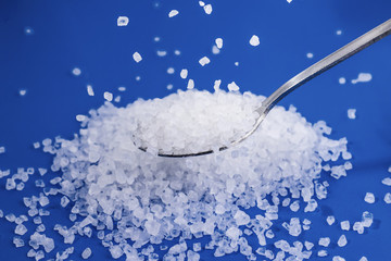 Coarse sea salt in a spoon. Some salt crystals pour on top