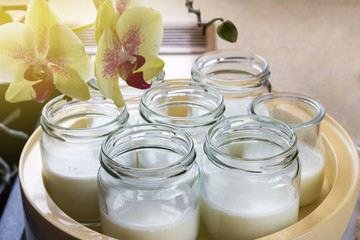 Glass jars with natural homemade organic yogurt in yogurt maker. Nearby is a delicate pink orchid flower.